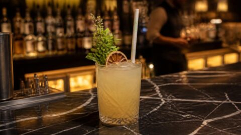 Craft cocktail with a sleek compostable straw on a dark marble bar counter in Sydney