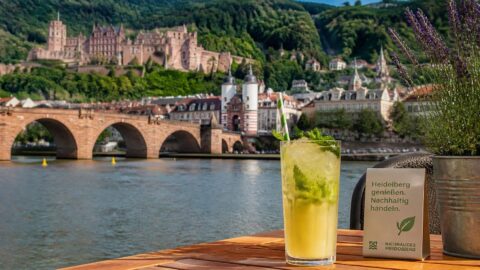 Refreshing beverage with a paper straw at a riverside café in Heidelberg with the historic castle in the background